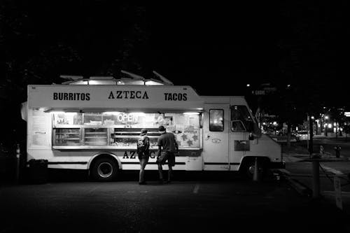 Фотография двух человек, стоящих перед грузовиком с едой в оттенках серого