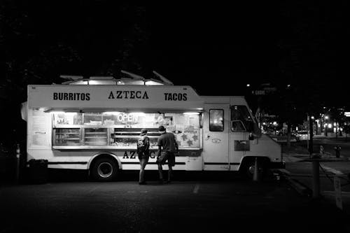 Fotografía En Escala De Grises De Dos Personas De Pie Frente A Un Camión De Comida