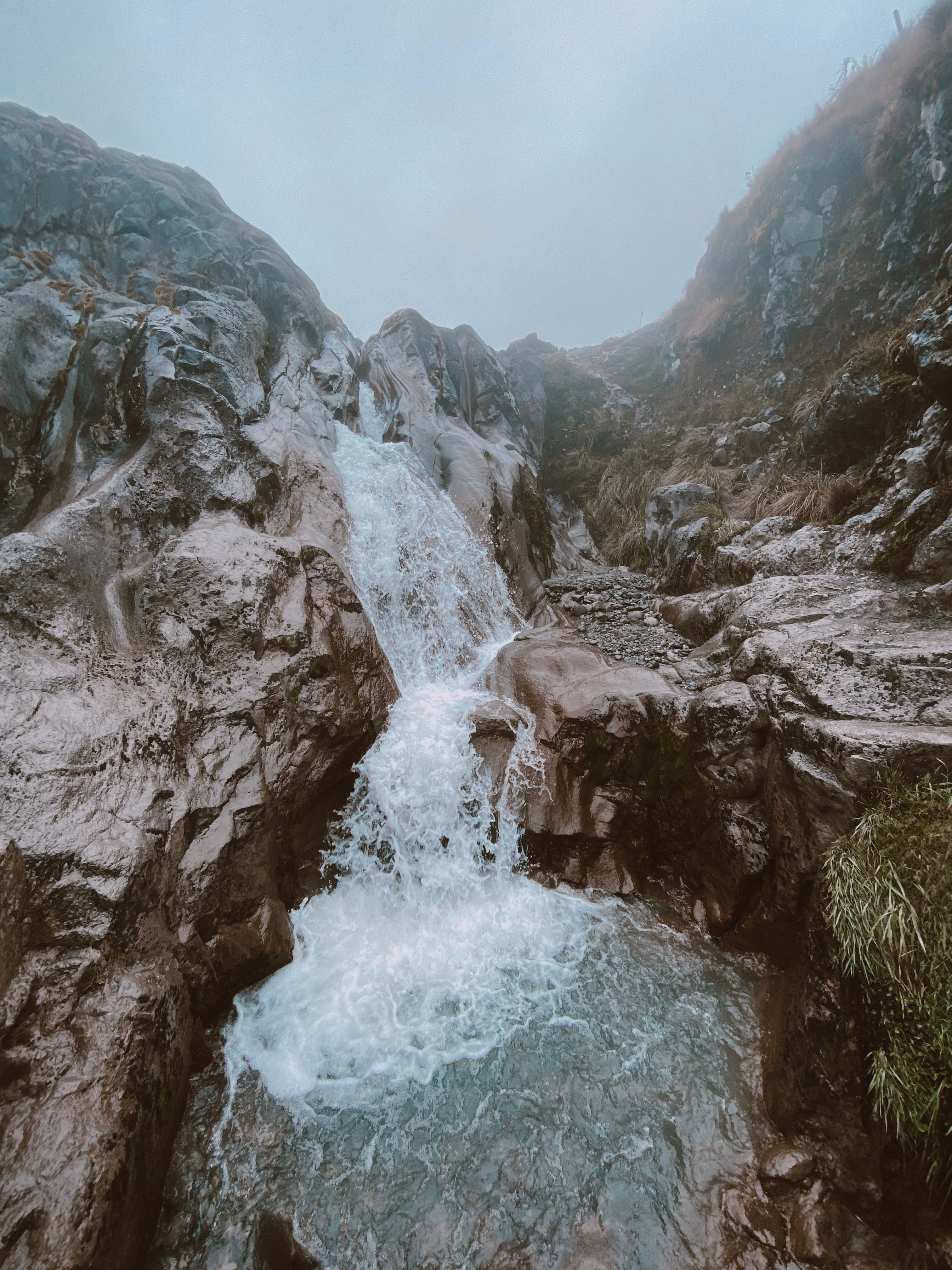 A scenic waterfall in the rocky terrain of Manizales, Colombia, under a misty sky.
