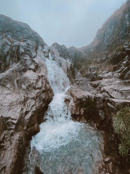 A scenic waterfall in the rocky terrain of Manizales, Colombia, under a misty sky.