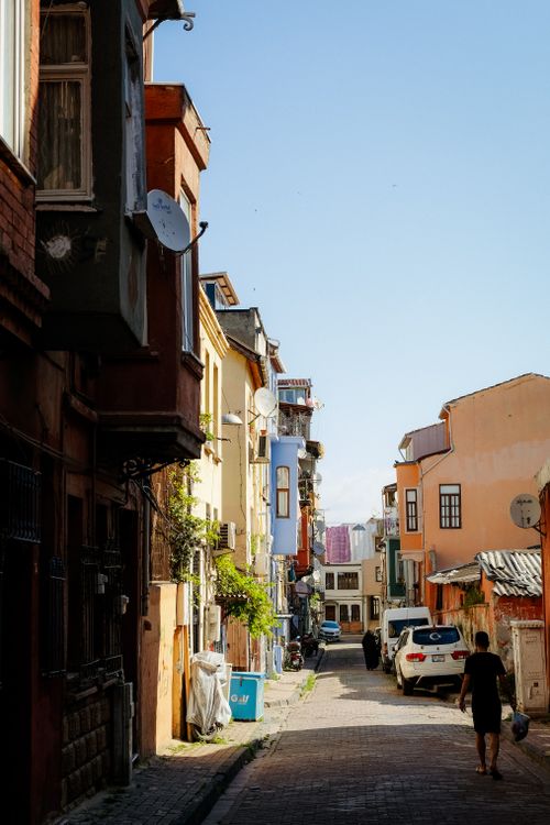 Free A vibrant urban alley featuring colorful buildings, parked cars, and a pedestrian walking on a sunny day. Stock Photo