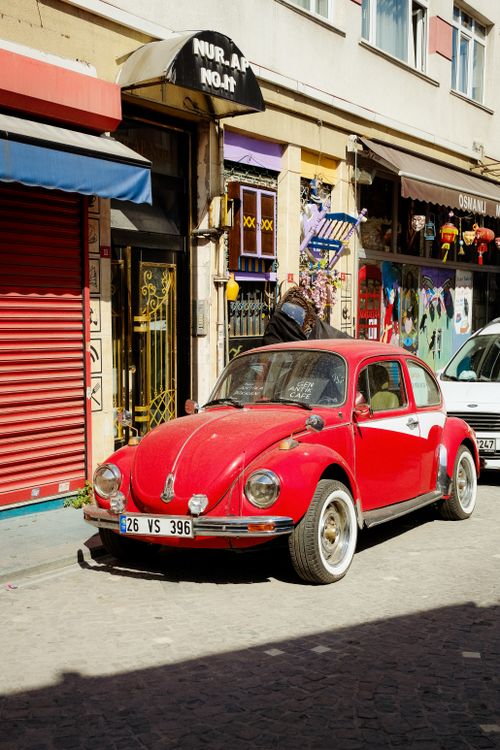 Free Classic red Volkswagen Beetle parked on a sunny street lined with colorful shops. Stock Photo