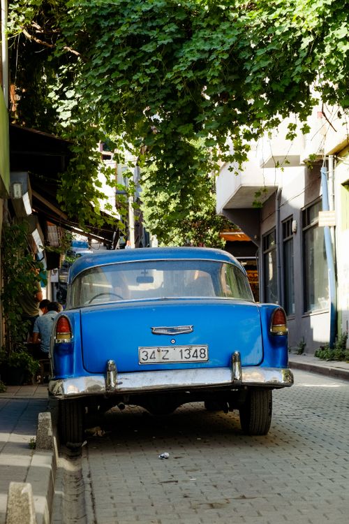 Free Classic blue car parked on a sunny, leafy street with a charming urban vibe. Stock Photo