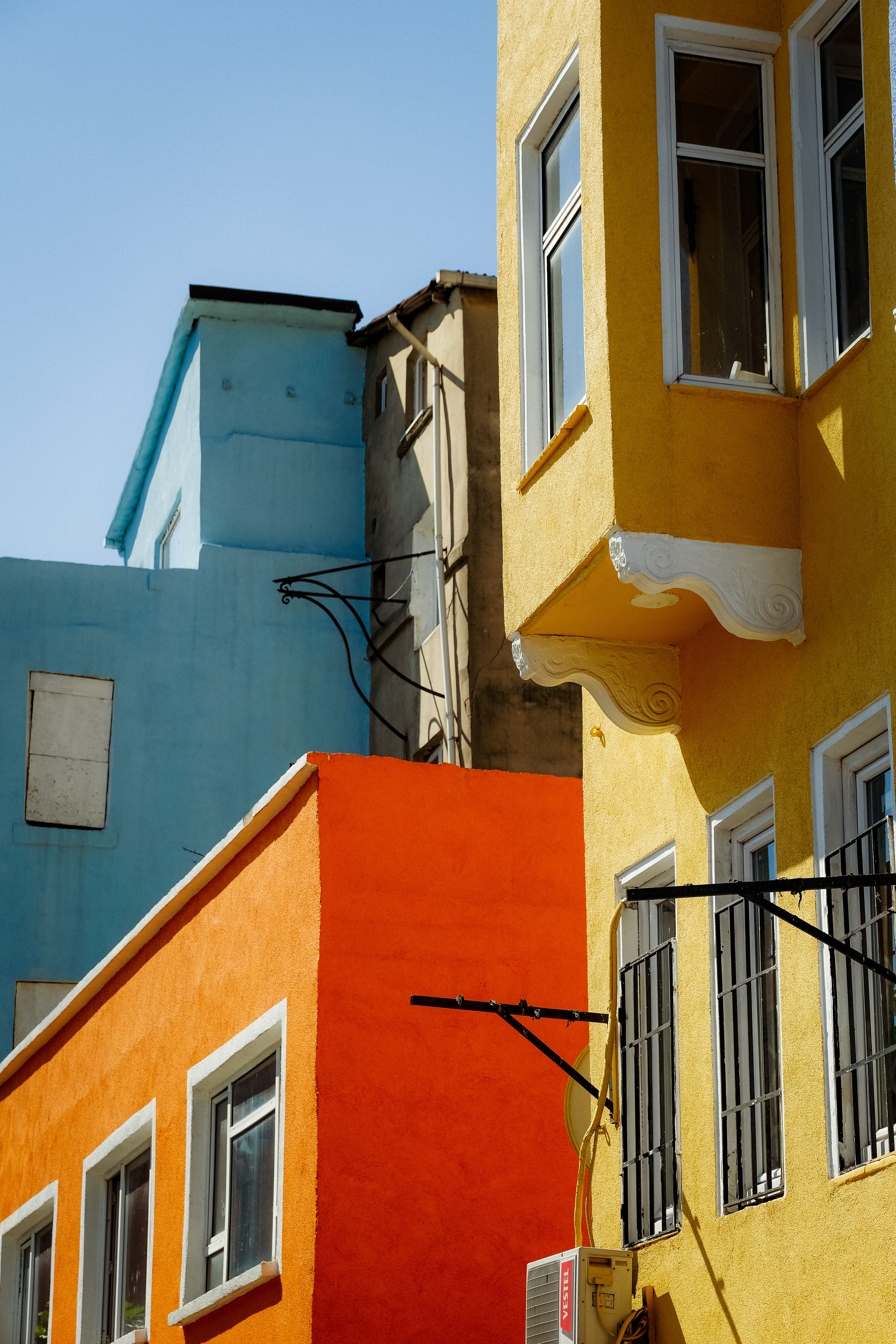 Fotomural Fachadas vibrantes de edificios contra un cielo azul claro en un entorno urbano.