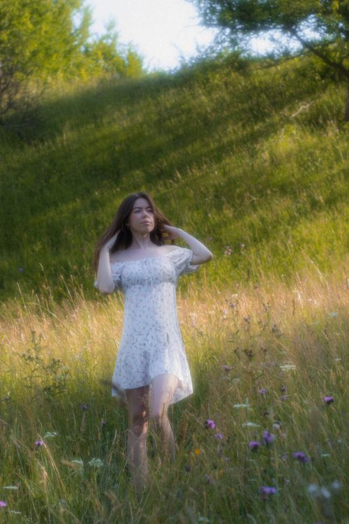 Free A serene portrait of a woman walking in a sunlit meadow with wildflowers. Stock Photo