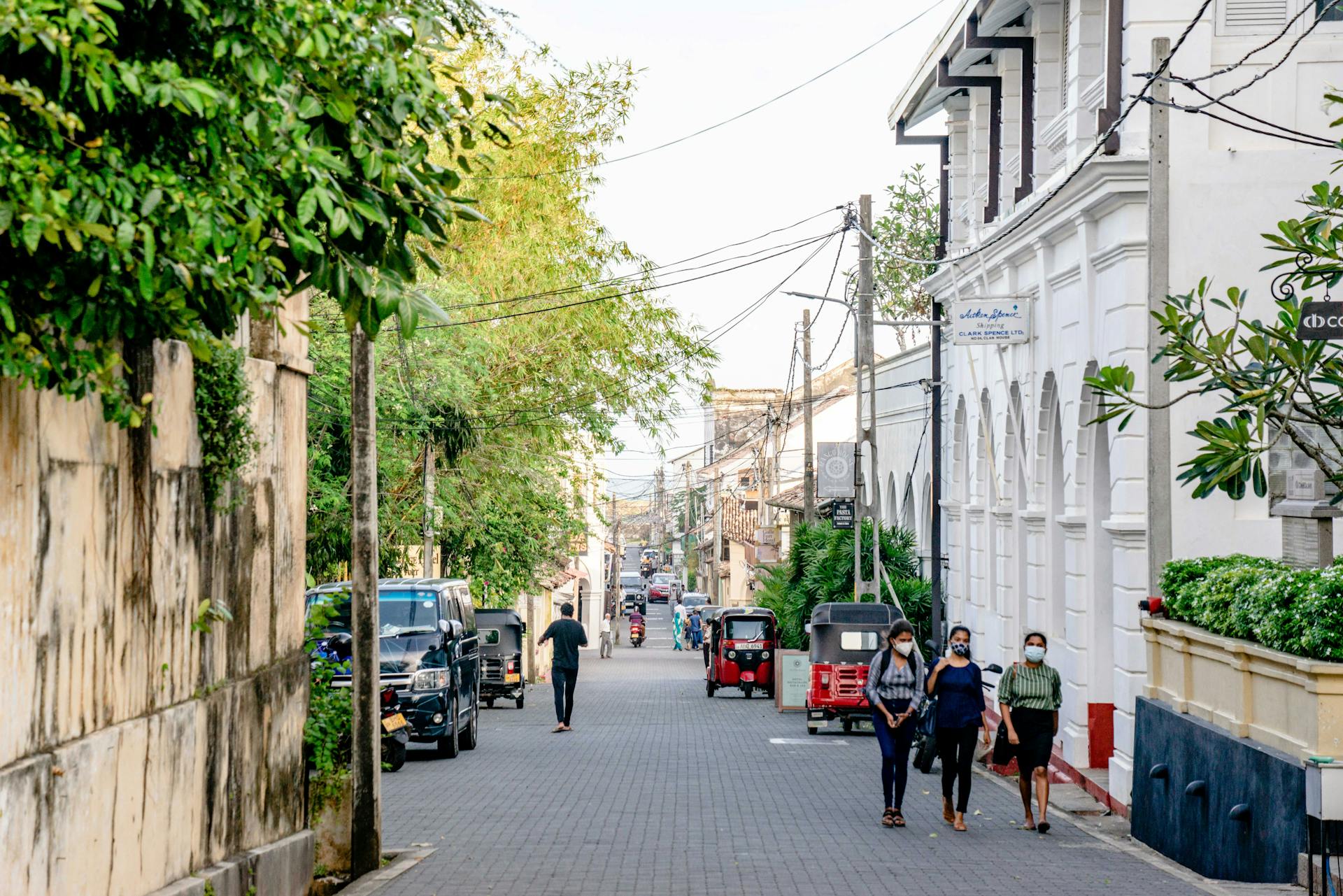Street in Galle Fort, Sri Lanka with people wearing masks, tuk-tuks, and colonial architecture.