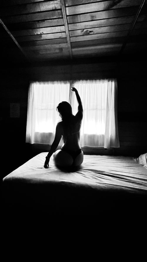 Free Elegant silhouette of a model sitting on a bed with raised arm in monochrome tones. Stock Photo