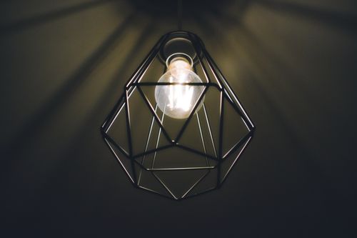 Free A modern geometric pendant light bulb in a dark room, casting warm, soothing illumination. Stock Photo