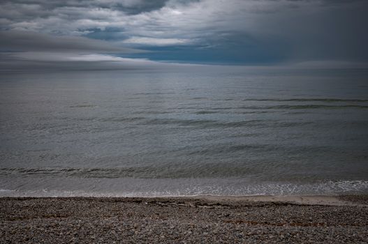 A tranquil beach scene with a cloudy sky over a calm ocean, creating a moody atmosphere.