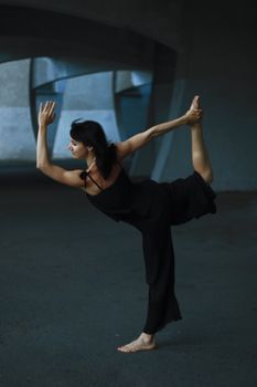 A woman gracefully balances in a yoga pose in a dark urban environment.