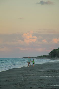 A father and son walk together on a serene beach at sunset, enjoying quality time.