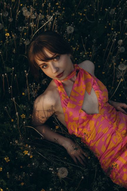 A woman in a pink patterned dress posing elegantly in a lush meadow.
