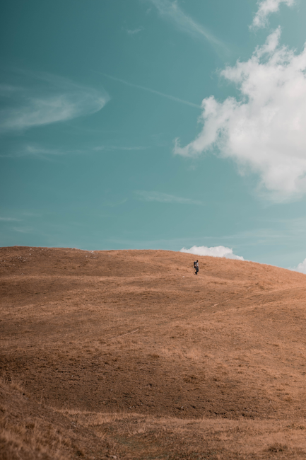 A lone person walking on a grassy hill under a clear blue sky, ideal for adventure themes.