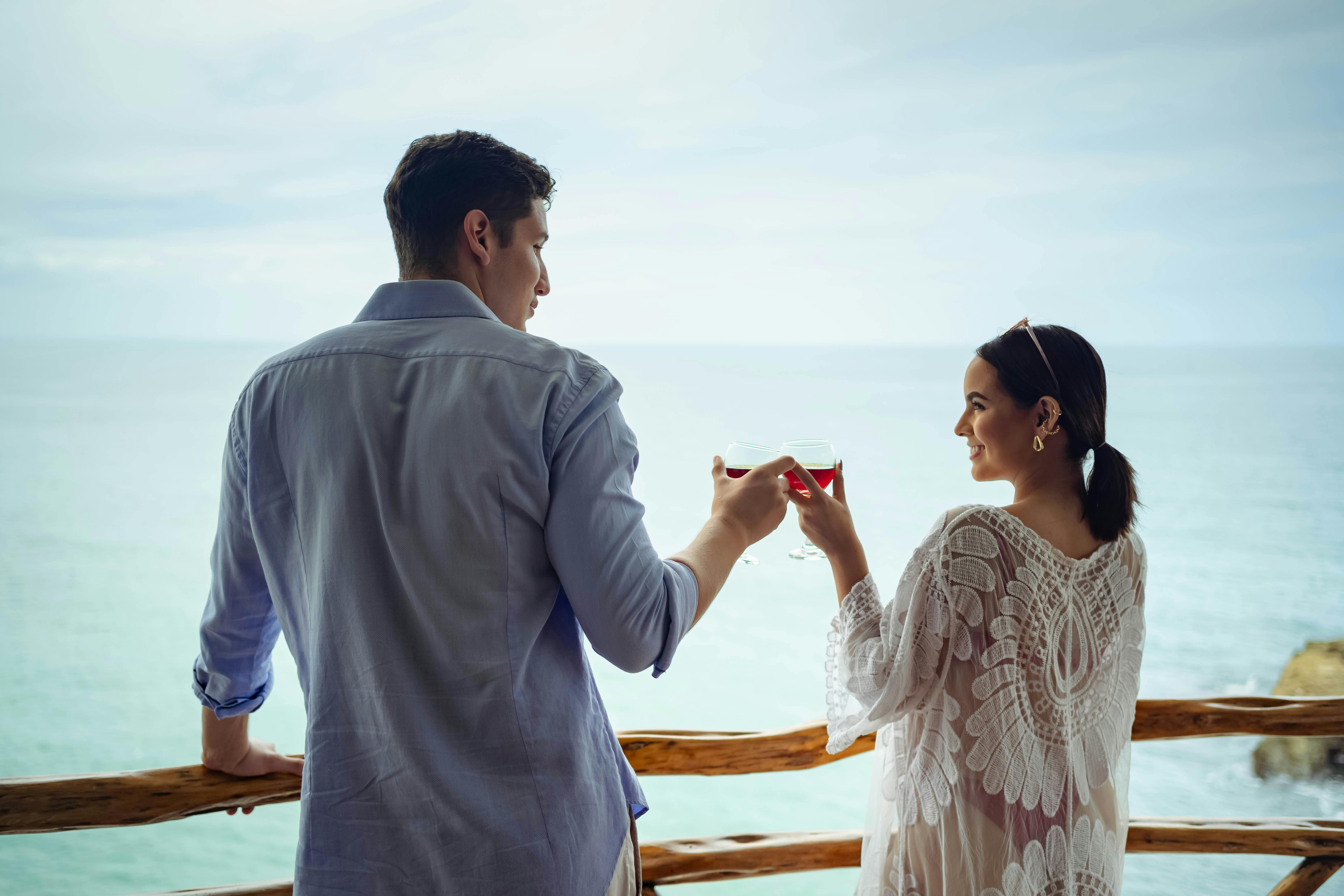 A couple enjoys a romantic moment with wine overlooking the ocean on a sunny day.