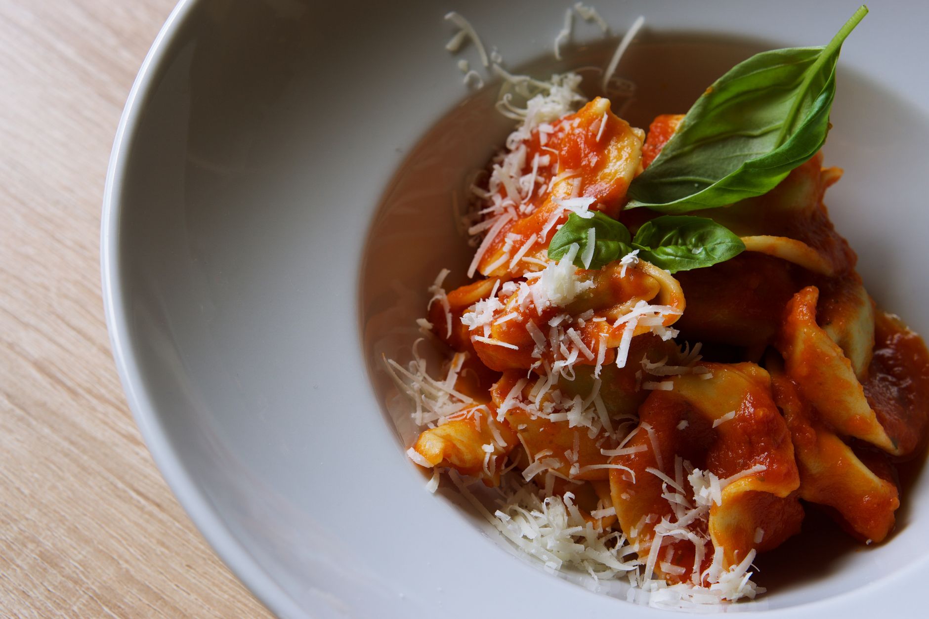A white bowl containing penne pasta coated in bright red arrabbiata sauce, garnished with fresh basil leaves and grated Parmigiano-Reggiano cheese