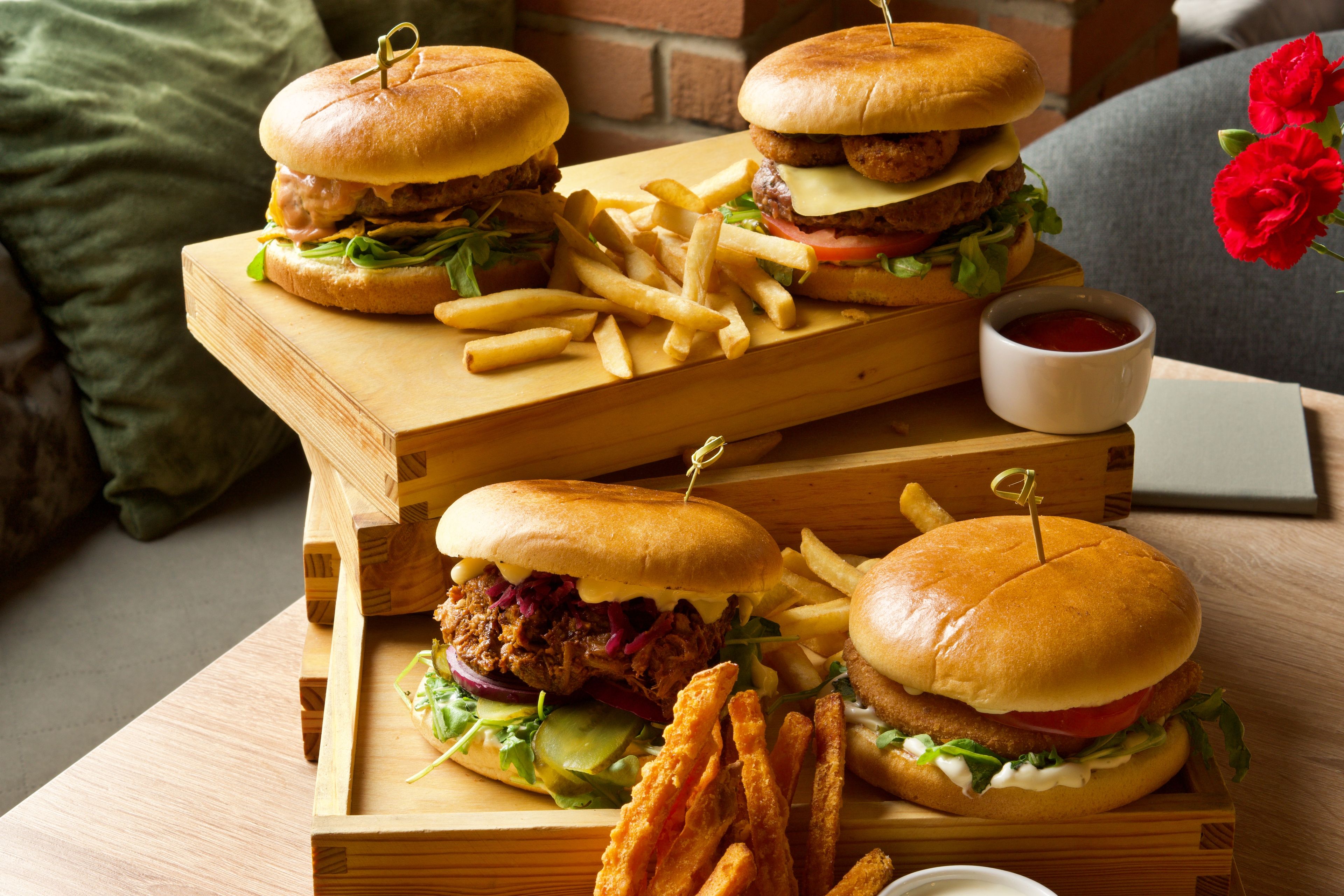 Three gourmet burgers with crispy fries on wooden trays, perfect for a delicious meal.