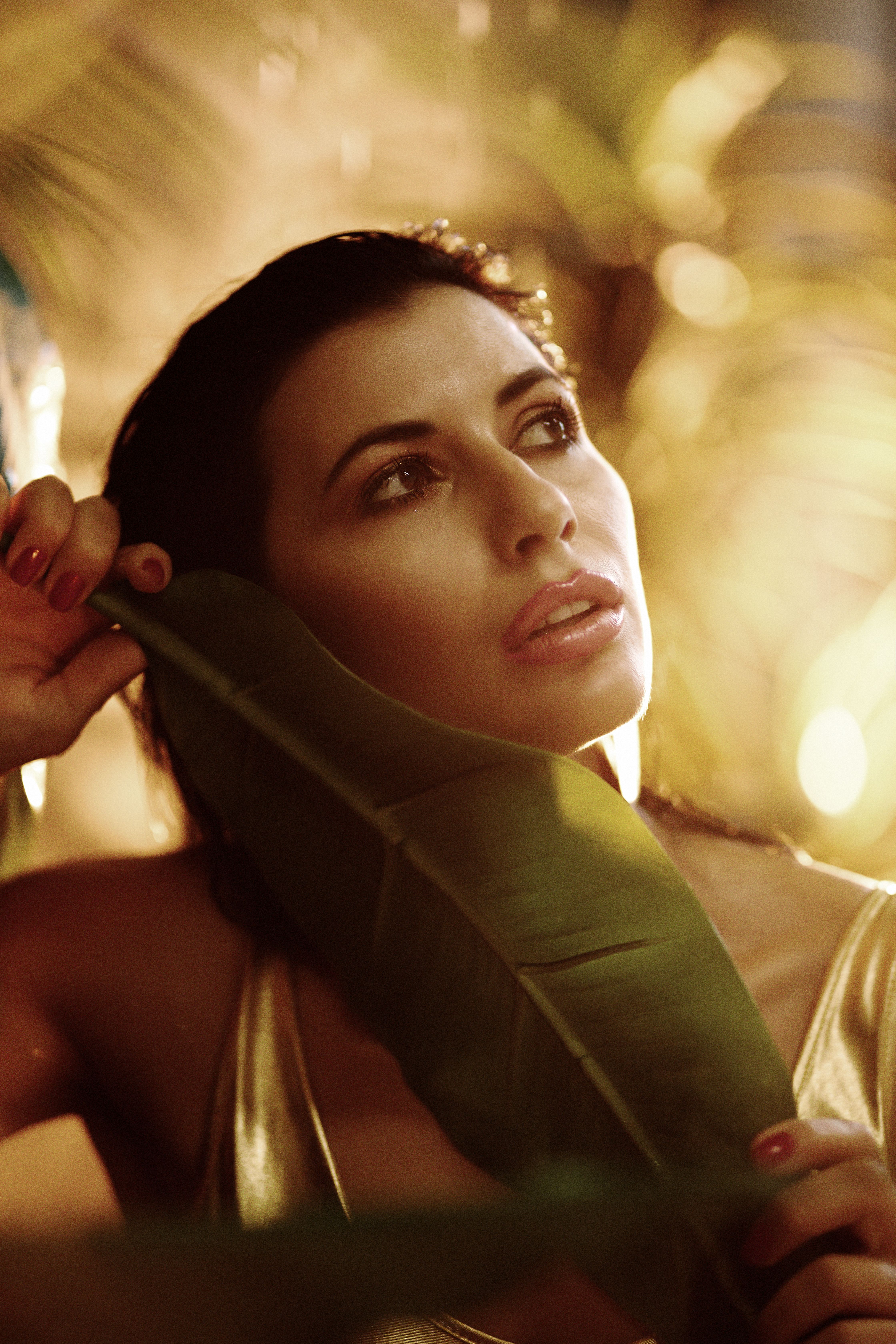 A beautiful woman poses with a tropical leaf in warm, atmospheric lighting, evoking a sense of seren