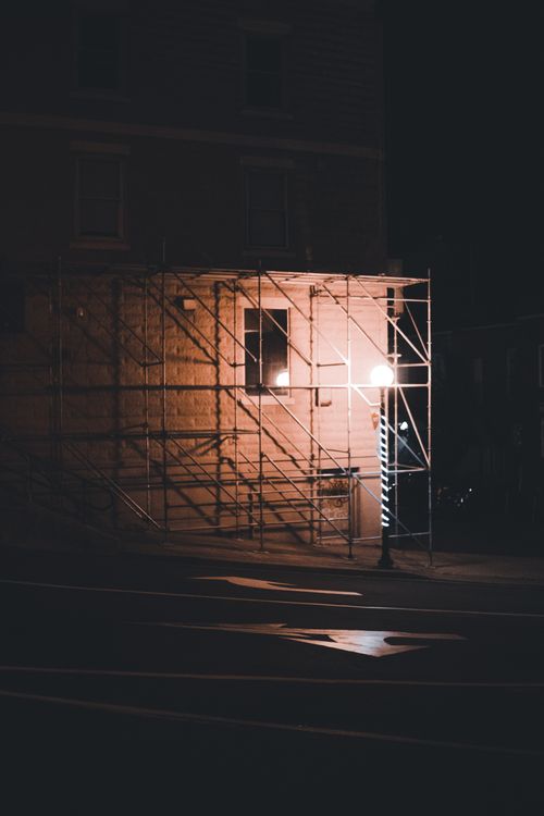 Free A dimly lit urban street corner featuring a building under construction with visible scaffolding and streetlights at night. Stock Photo