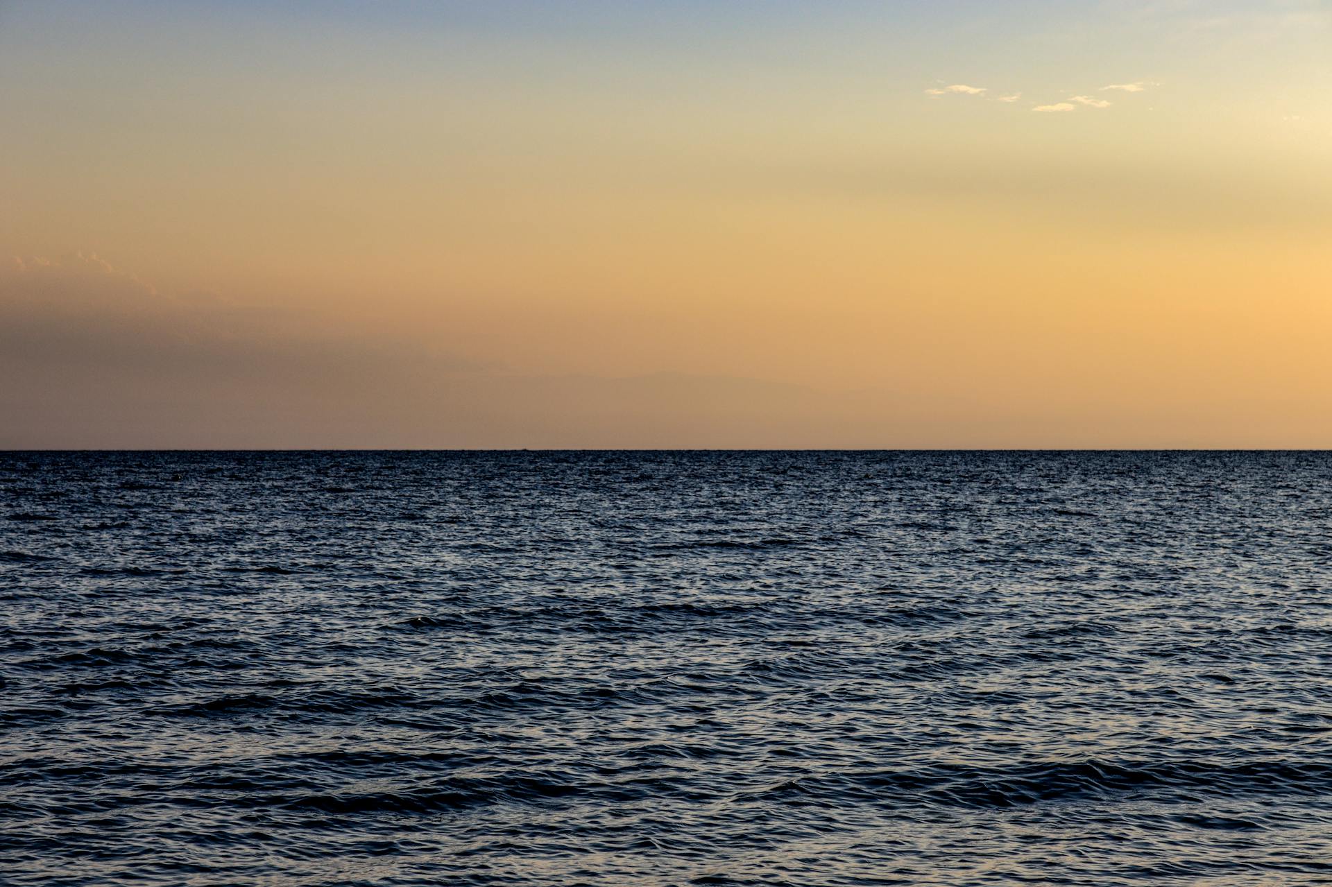 Peaceful seascape at sunset in Nea Irakleia, Greece with calm waves and an orange sky.