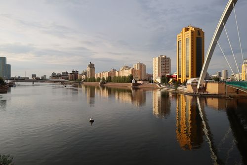 Free A serene cityscape with buildings reflecting on a calm river at dusk. Stock Photo