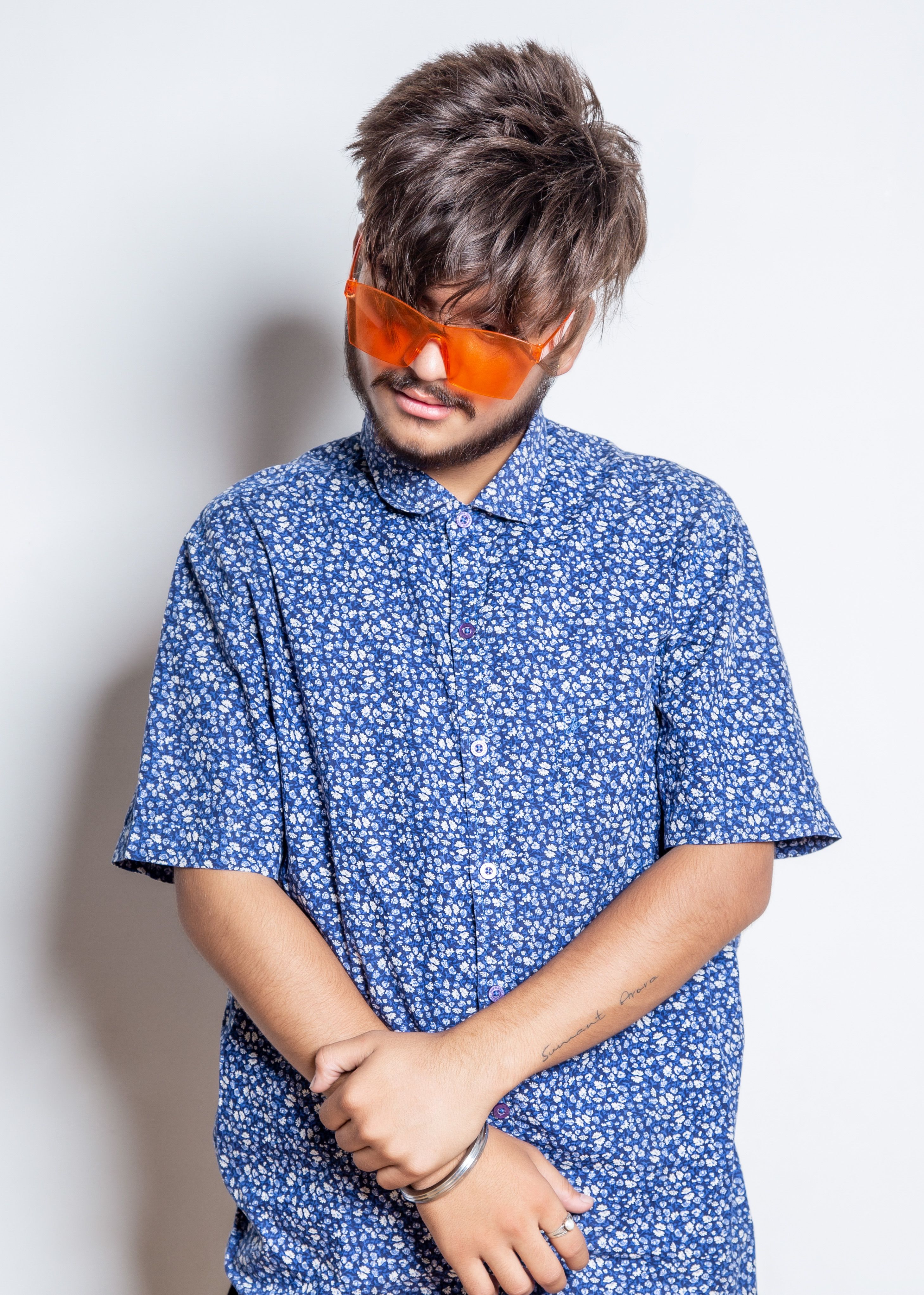Stylish man wearing orange sunglasses and floral shirt, exuding a modern fashion vibe.