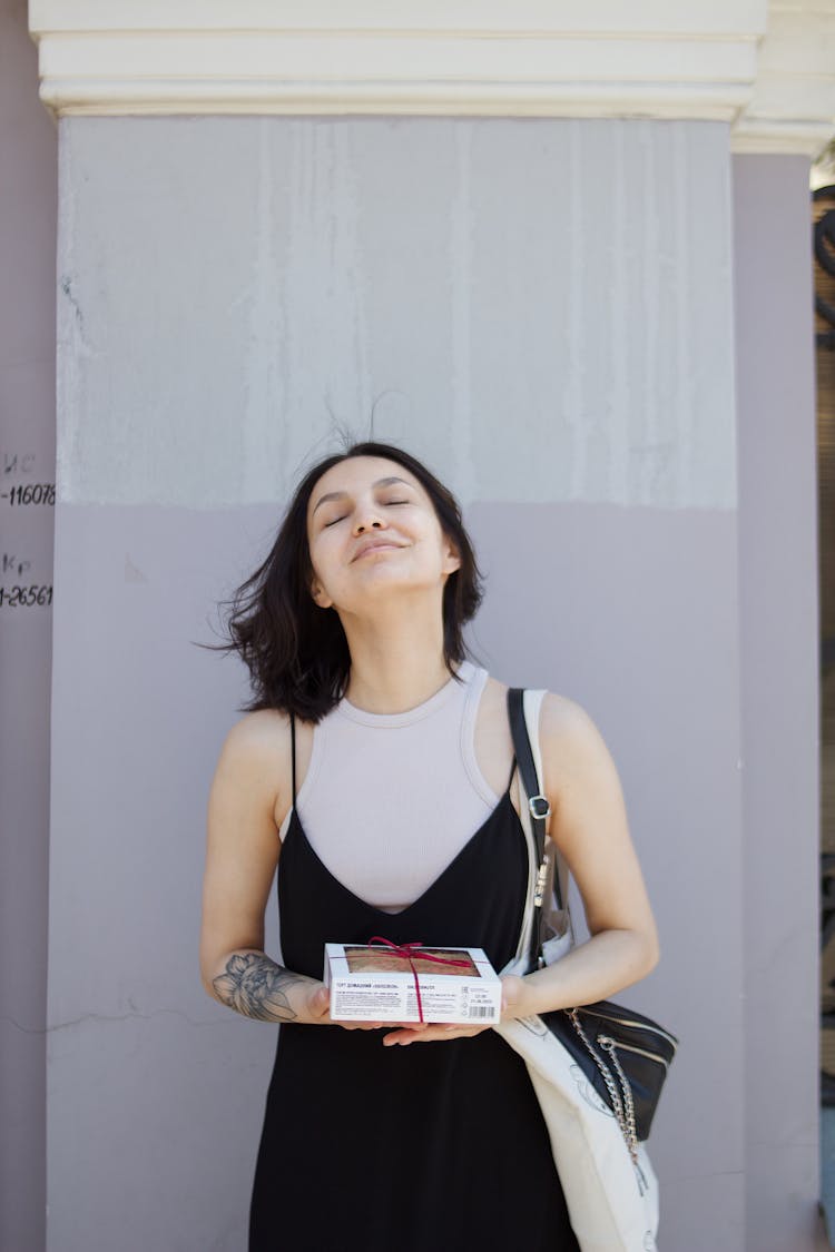 A Woman In Black Dress Holding A Box With Her Eyes Closed