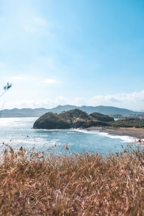 Free A picturesque view of a serene coastline with a rocky island surrounded by clear blue waters. Stock Photo