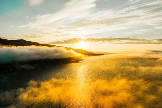 A breathtaking sunset over the Norwegian coastline with vibrant golden hues and clouds.