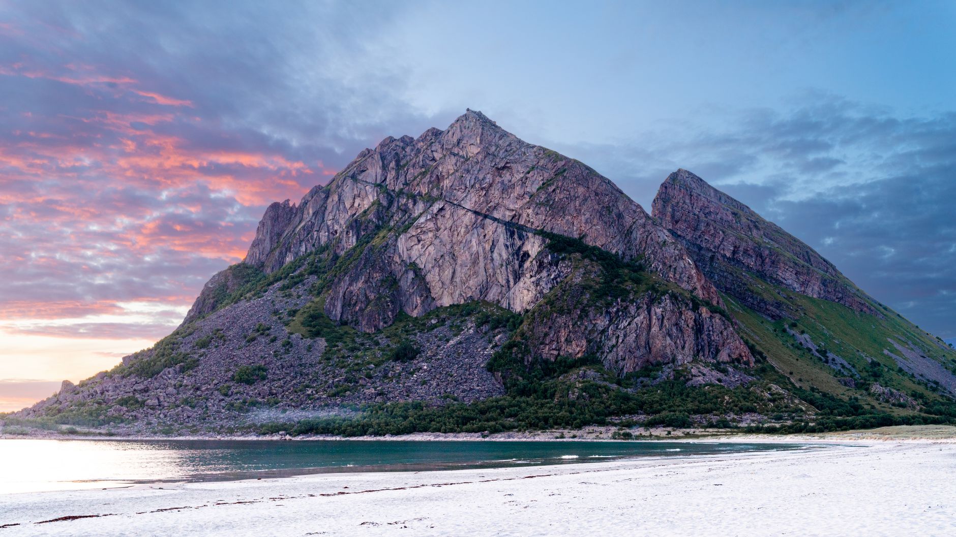 A breathtaking view of a rock formation on a white sand beach in Nordland, Norway at sunset.