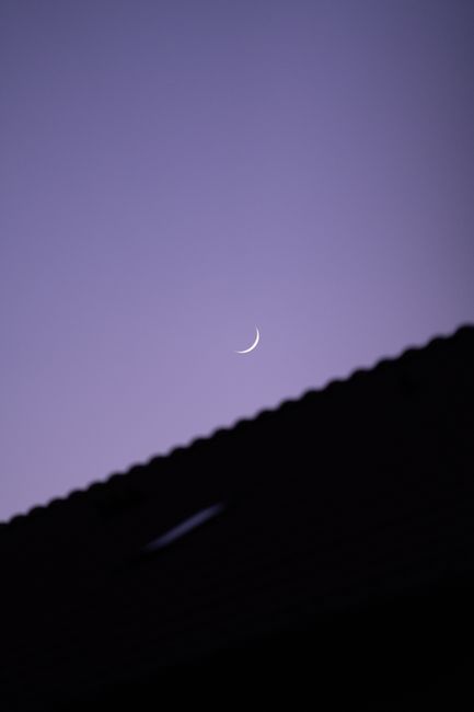 Captivating crescent moon above a silhouetted rooftop during twilight in Norway.
