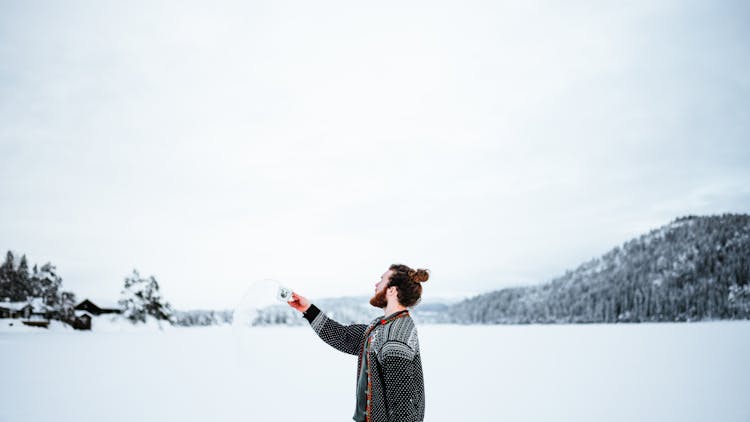 Man Standing Outside In Winter And Throwing Water From A Cup 