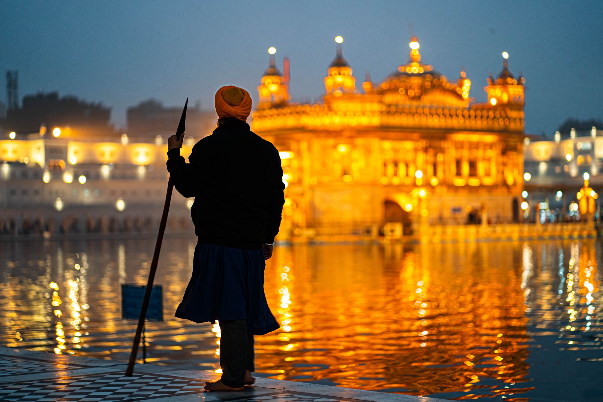 Silhouette of Sikh man holding spear at Golden Temple, Amritsar during twilight reflection view.
