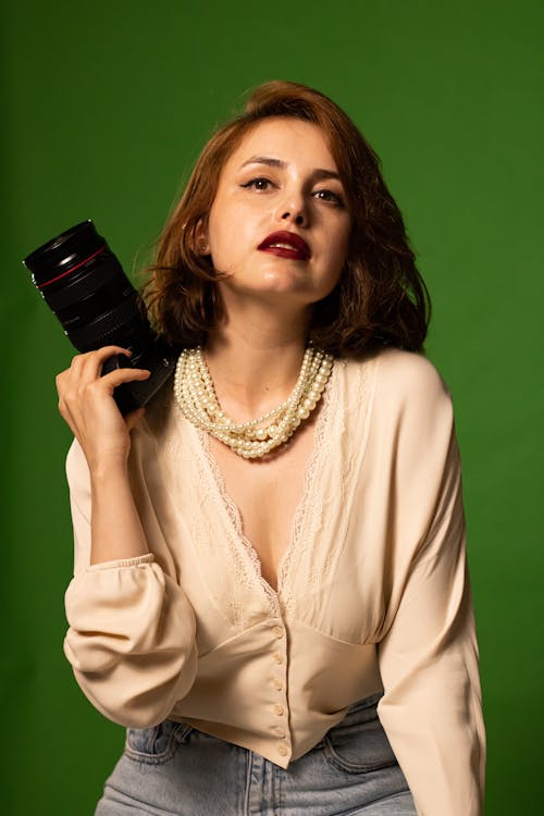 A Woman in Beige Long Sleeves Wearing a Pearl Necklace while Holding a Camera Lens