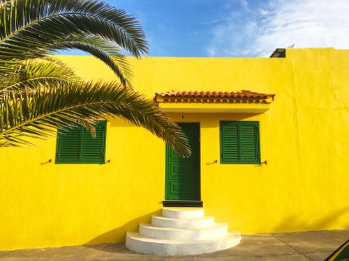 Free Vibrant yellow house facade in Spain with green shutters and a palm tree. Stock Photo