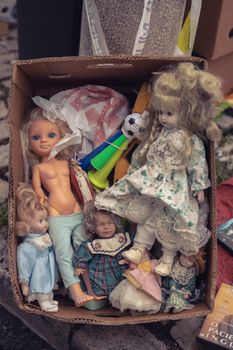 A collection of vintage dolls and toys in a cardboard box placed outdoors.