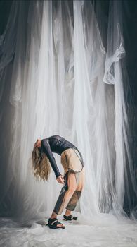 Creative fashion portrait featuring a woman bending in an ethereal setting with flowing fabrics.