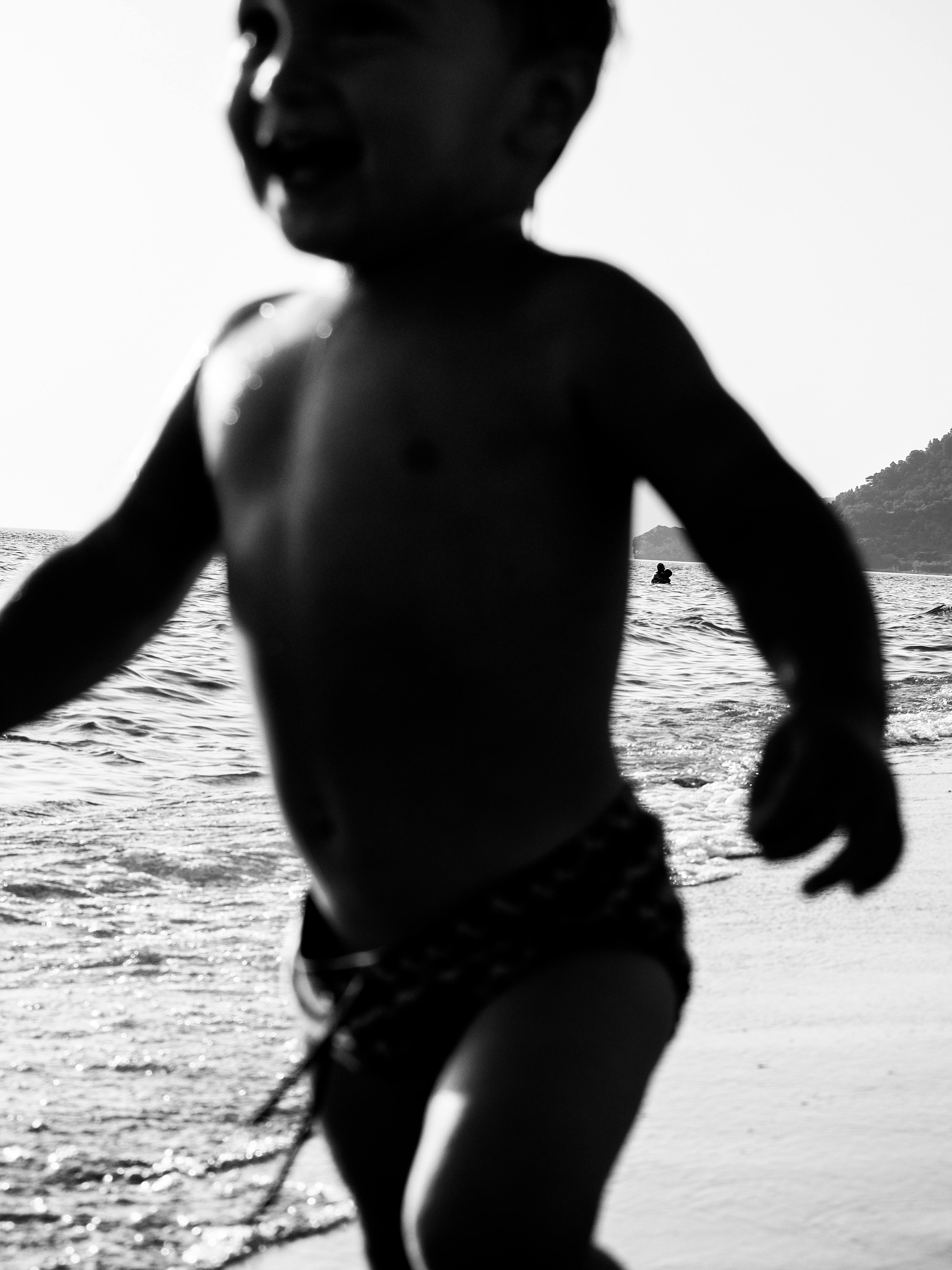 grayscale photo of a shirtless kid near the body of water