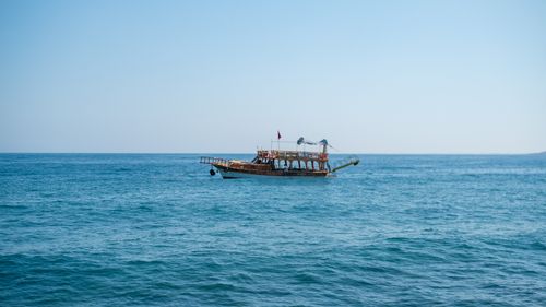 Free A serene view of a wooden boat sailing on the calm ocean waters under a clear blue sky. Stock Photo