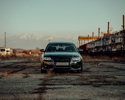 A sleek black Audi A3 sedan parked on an old industrial road with mountains in the background.