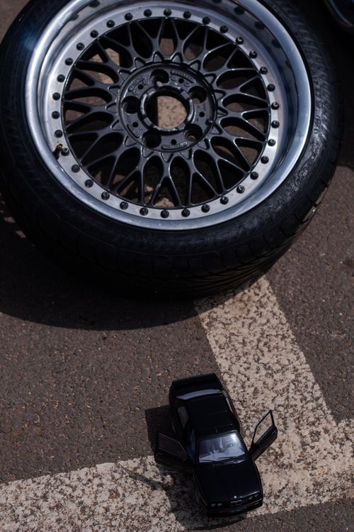 Free Close-up view of a toy car next to a large tire rim on an asphalt surface. Stock Photo