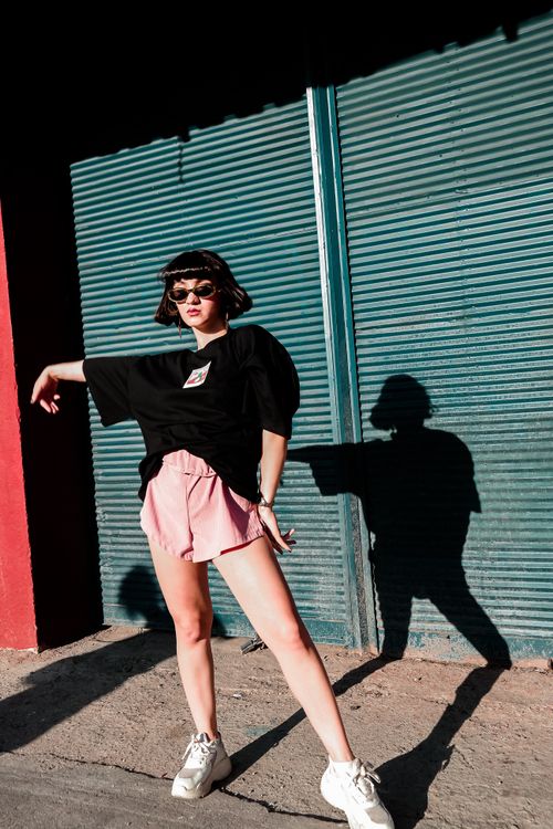 Free Fashionable woman in sunglasses and shorts posing outdoors with dramatic shadow. Stock Photo