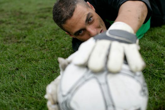 Dynamic shot of a goalkeeper reaching for a soccer ball on a grass field, showcasing sports dedication.