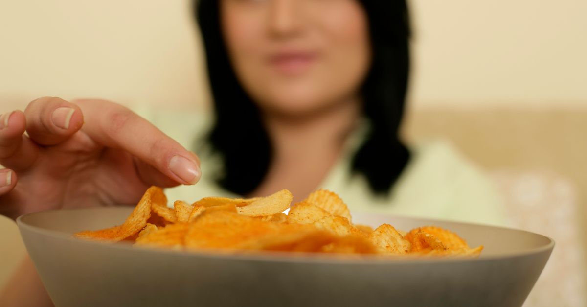 Person reaching for junk food with tired eyes, clock in background showing late night