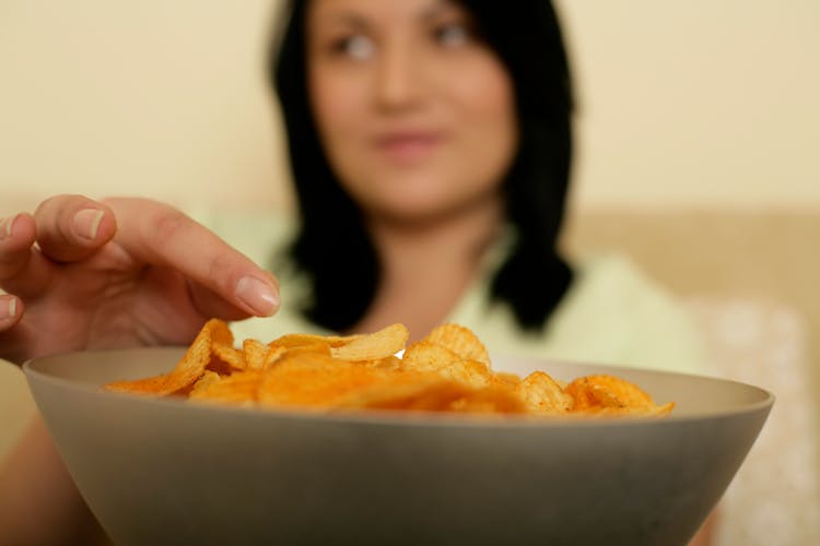 Photo Of A Bowl With Crisps And A Woman In The Background Reaching For The Crisps