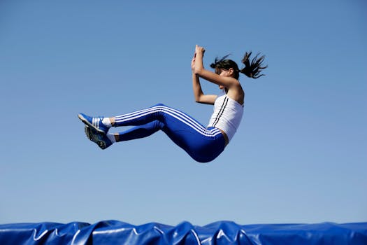 Female athlete in mid-air during athletic jump with blue sky background.