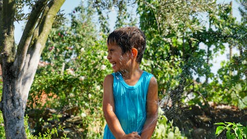 Photo of a Boy Laughing at Being Soaked in Water by a Garden Hose