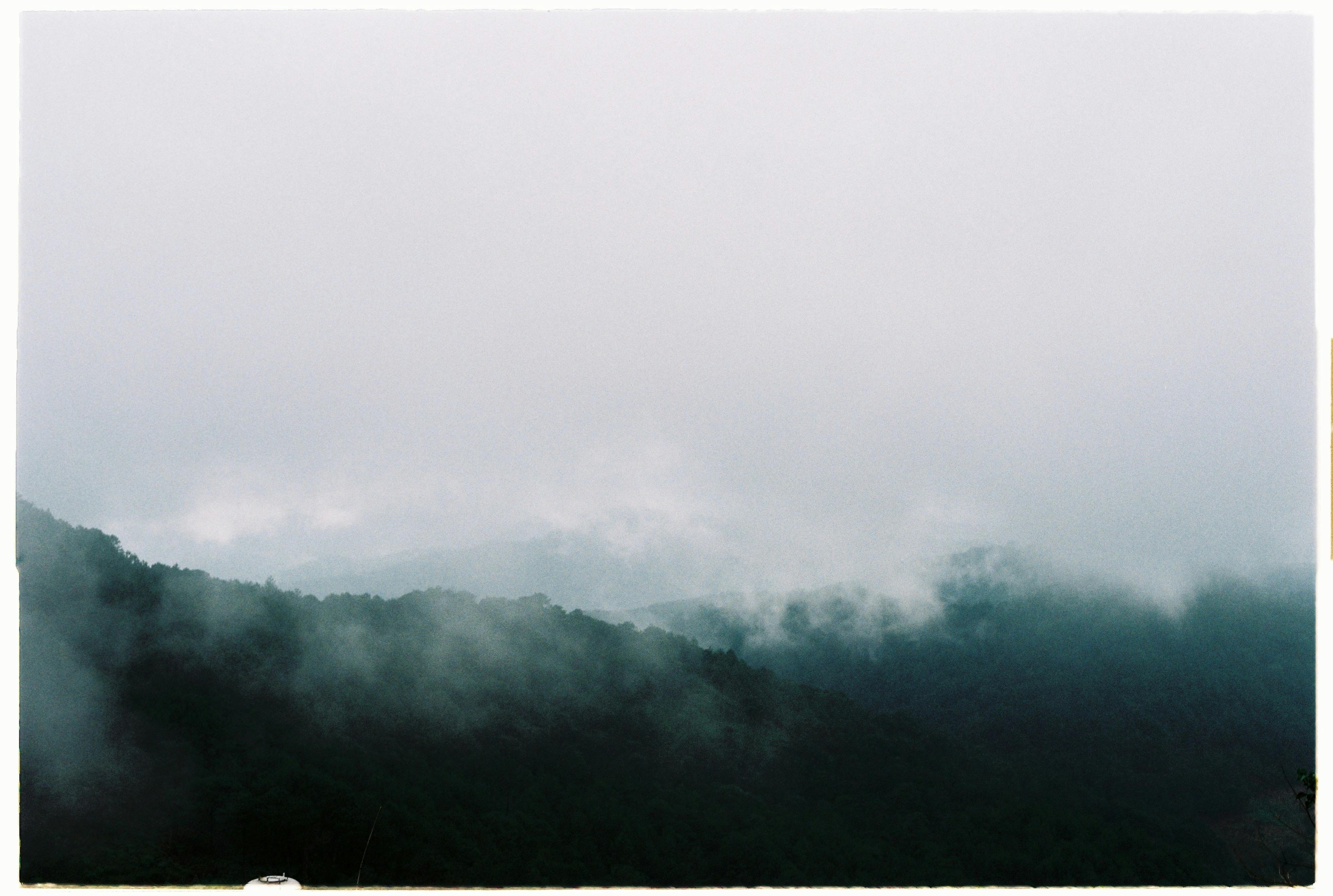 A serene and mysterious view of foggy mountains under a cloudy sky, evoking nostalgia and mystery.