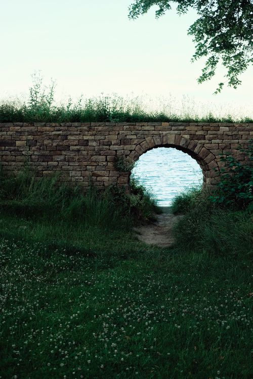 Free Tranquil scene of a brick archway open to a view of Denmark's shoreline with lush greenery. Stock Photo