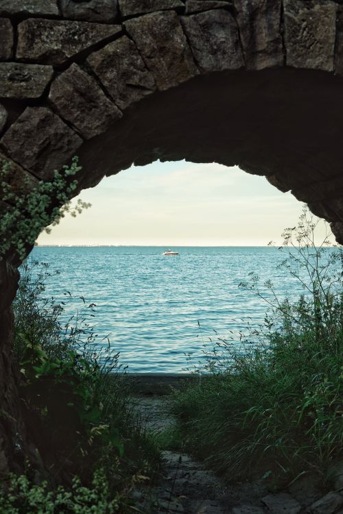 Free View of tranquil sea through a rustic stone archway, perfect blend of nature and architecture. Stock Photo