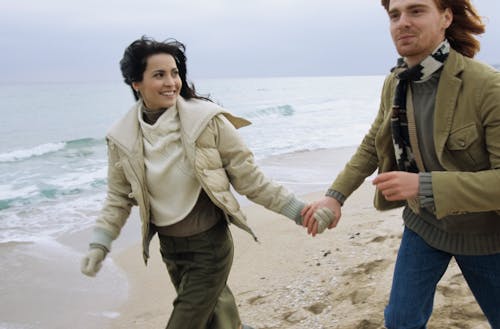 Free A Couple Walking on the Beach while Holding Hands Stock Photo